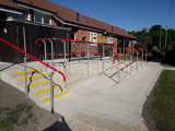 red powder coated handrail system places in pedestrian area. Disability Access Ramp access up to residential area 