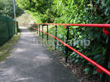 Railway station walkway with DDA disability handrails, powder coated in red and black. Green fence to the left hand side 